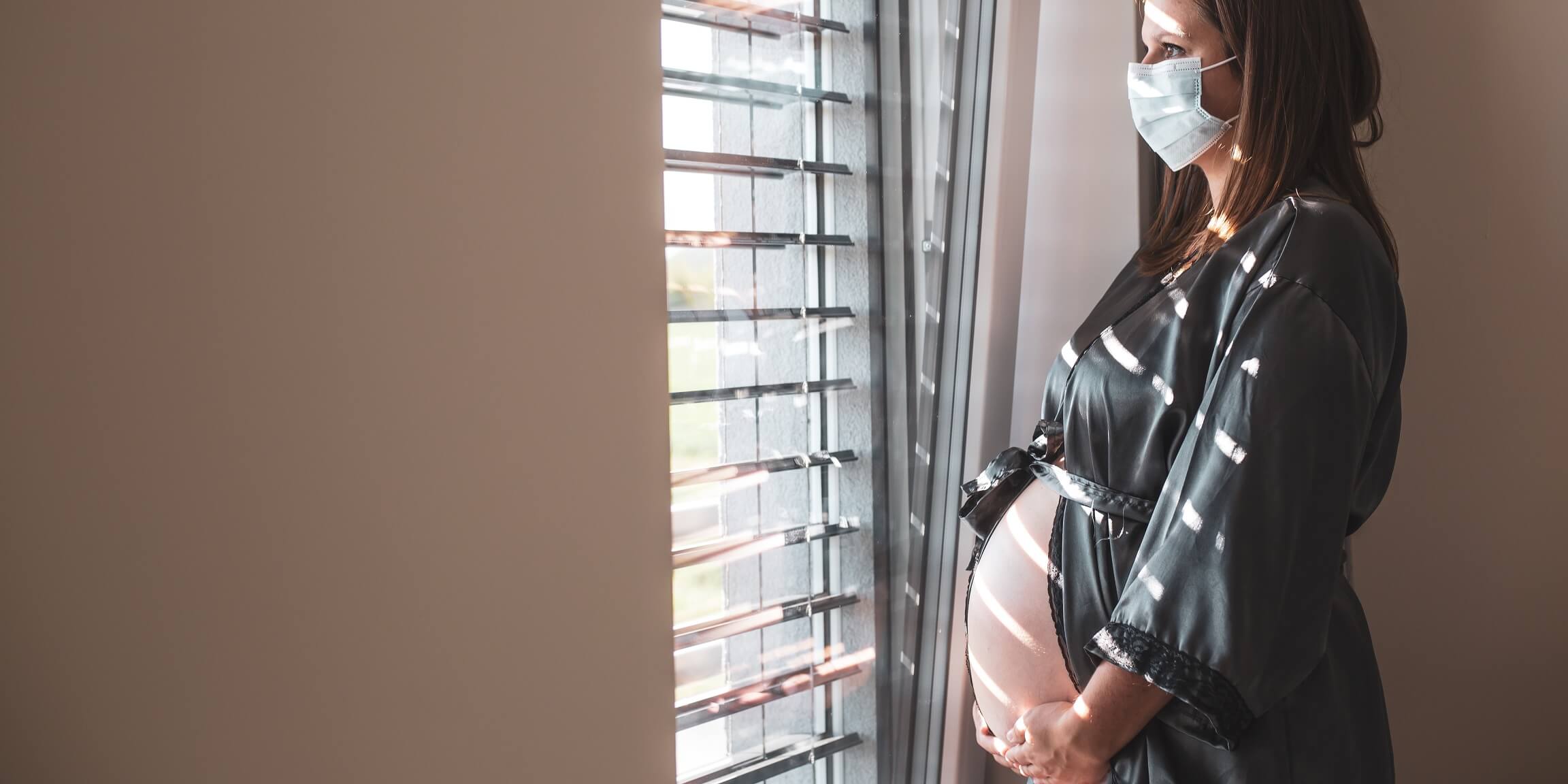 Schwangere Frau blickt aus dem Fenster